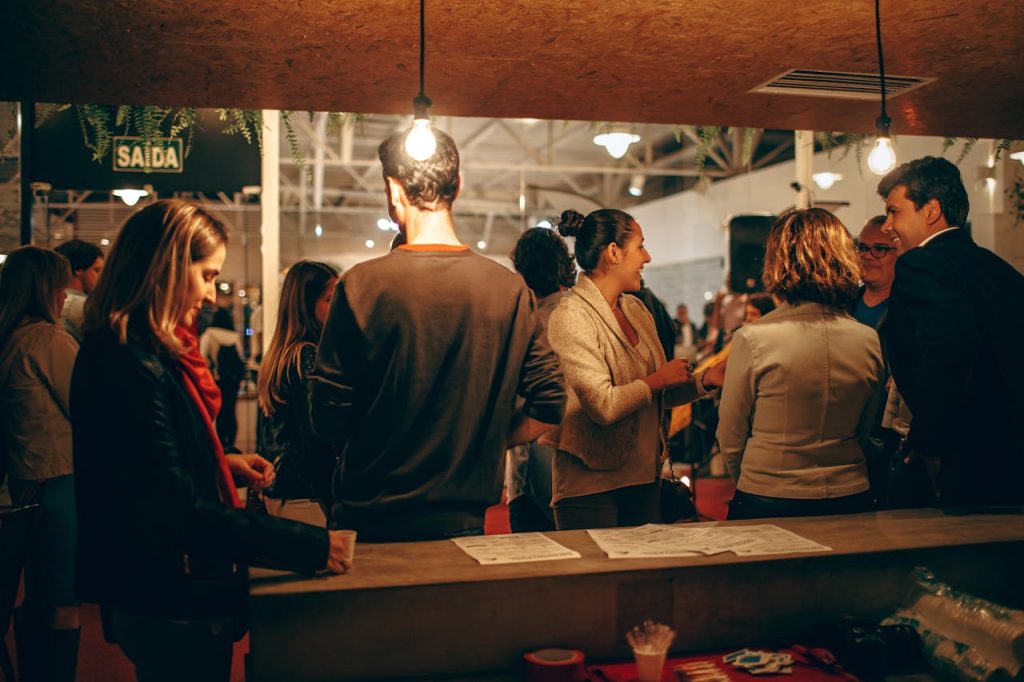 people-sitting-on-brown-wooden-bench-3700250 A lively indoor social gathering with people interacting warmly under cozy lighting.